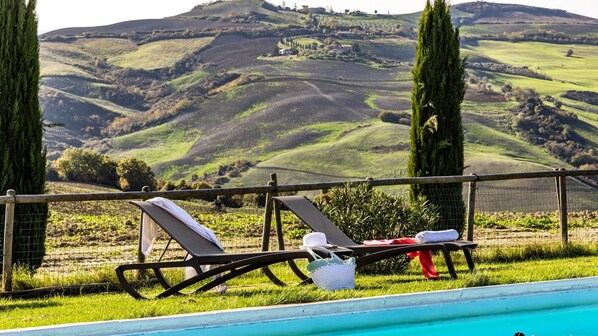 A poolside area with lounge chairs and a view of rolling hills. - Il Poggiarellino 14, Emma Villas (Volterra)