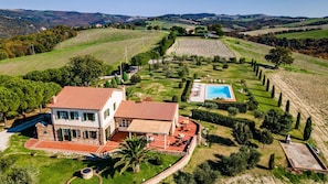Una casa grande con techo de tejas rojas, piscina y un jardín bien cuidado con setos y árboles.