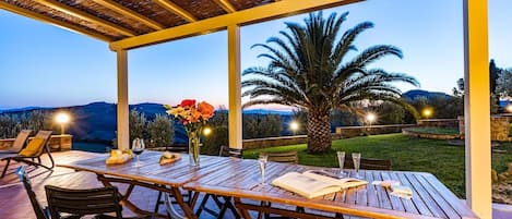 Un patio al aire libre con una mesa y sillas de madera, un jarrón de flores y vistas a las colinas.