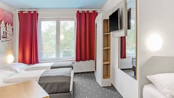 A hotel room with two beds, a TV, a desk, and a window with red curtains.