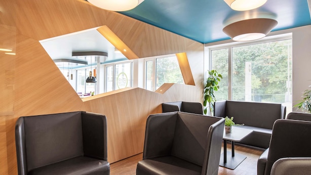 Een modern interieur met een houten accentmuur, zwarte lederen zitmogelijkheden en een groot raam met uitzicht op groen.
