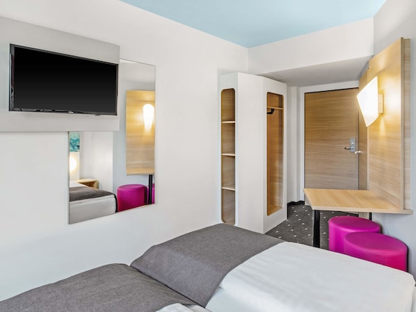 Une chambre d’hôtel moderne équipée d’un lit, d’un téléviseur fixé au mur, d’une armoire en bois et d’un petit bureau avec une chaise.
