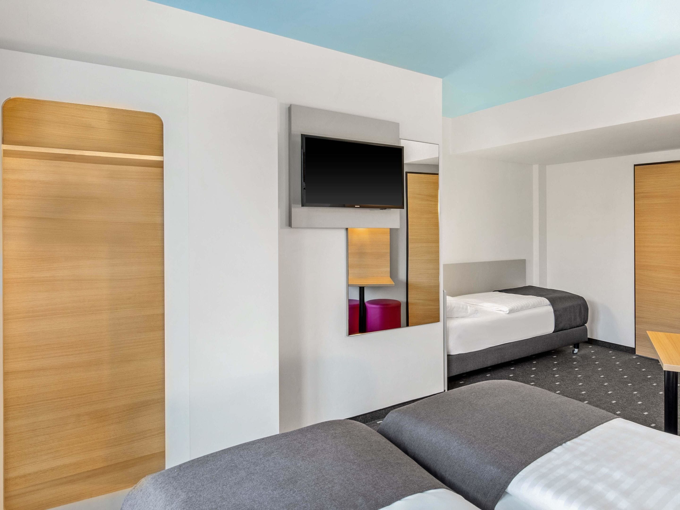 A modern hotel room with a bed, a TV mounted on the wall, and a wooden panel design.