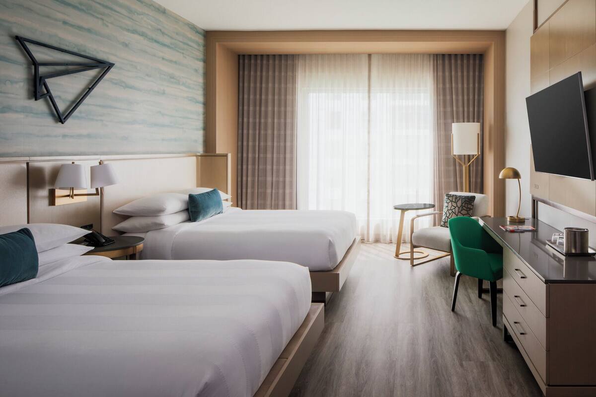 Habitació d'hotel amb dos llits, una taula de treball, una televisió i una finestra amb cortines.