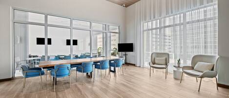 A modern conference room with a large table and blue chairs, large windows, and a flat-screen TV.