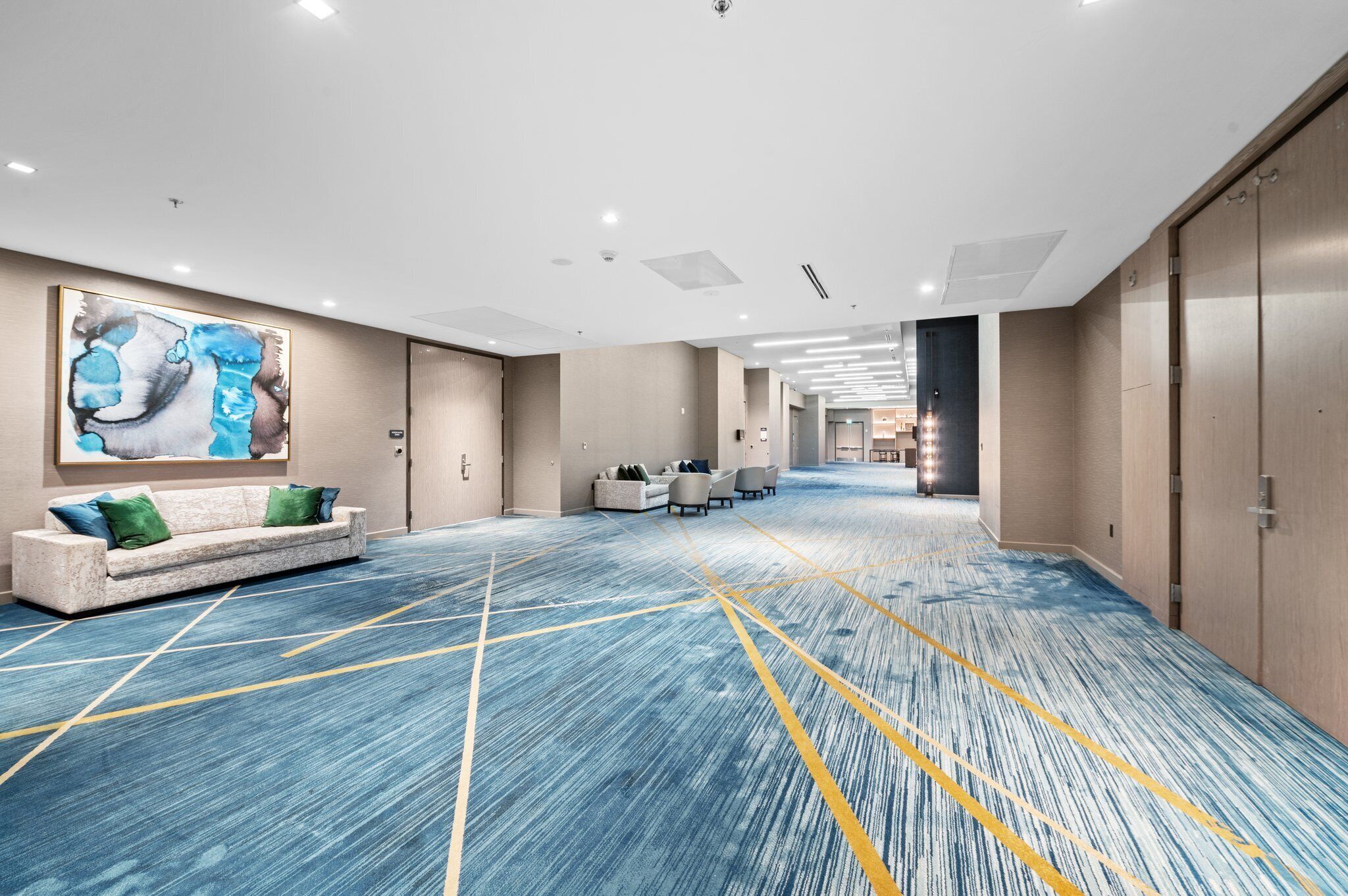 A spacious hotel lobby with a blue carpet, a sofa with green cushions, and a large abstract painting on the wall.