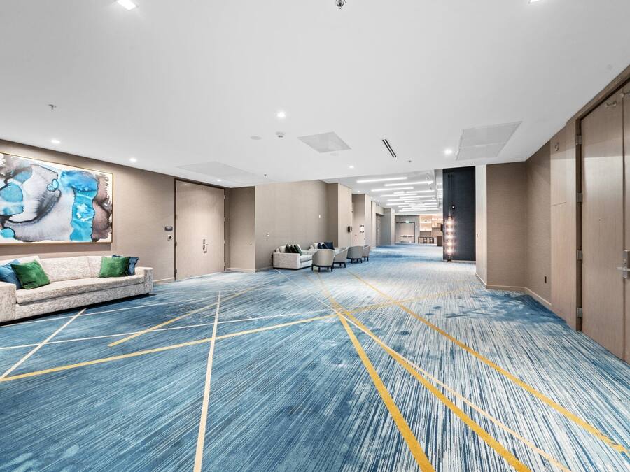 A spacious hotel lobby with a blue carpet, a sofa with green cushions, and a large abstract painting on the wall.