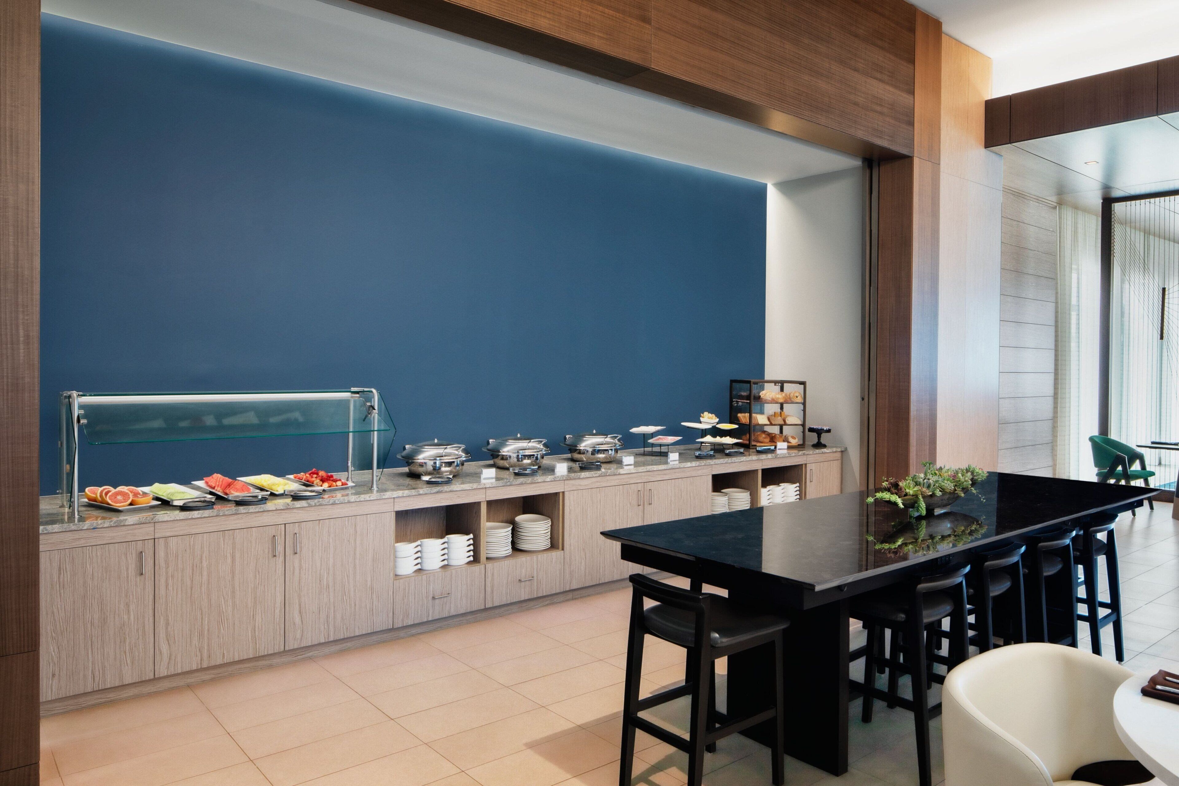 A modern breakfast bar with a blue accent wall, a variety of food options, and a seating area with bar stools.