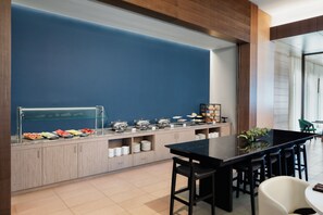 A modern breakfast bar with a blue accent wall, wooden cabinets, and a black table. - Marriott Fort Lauderdale Airport (Dania Beach)