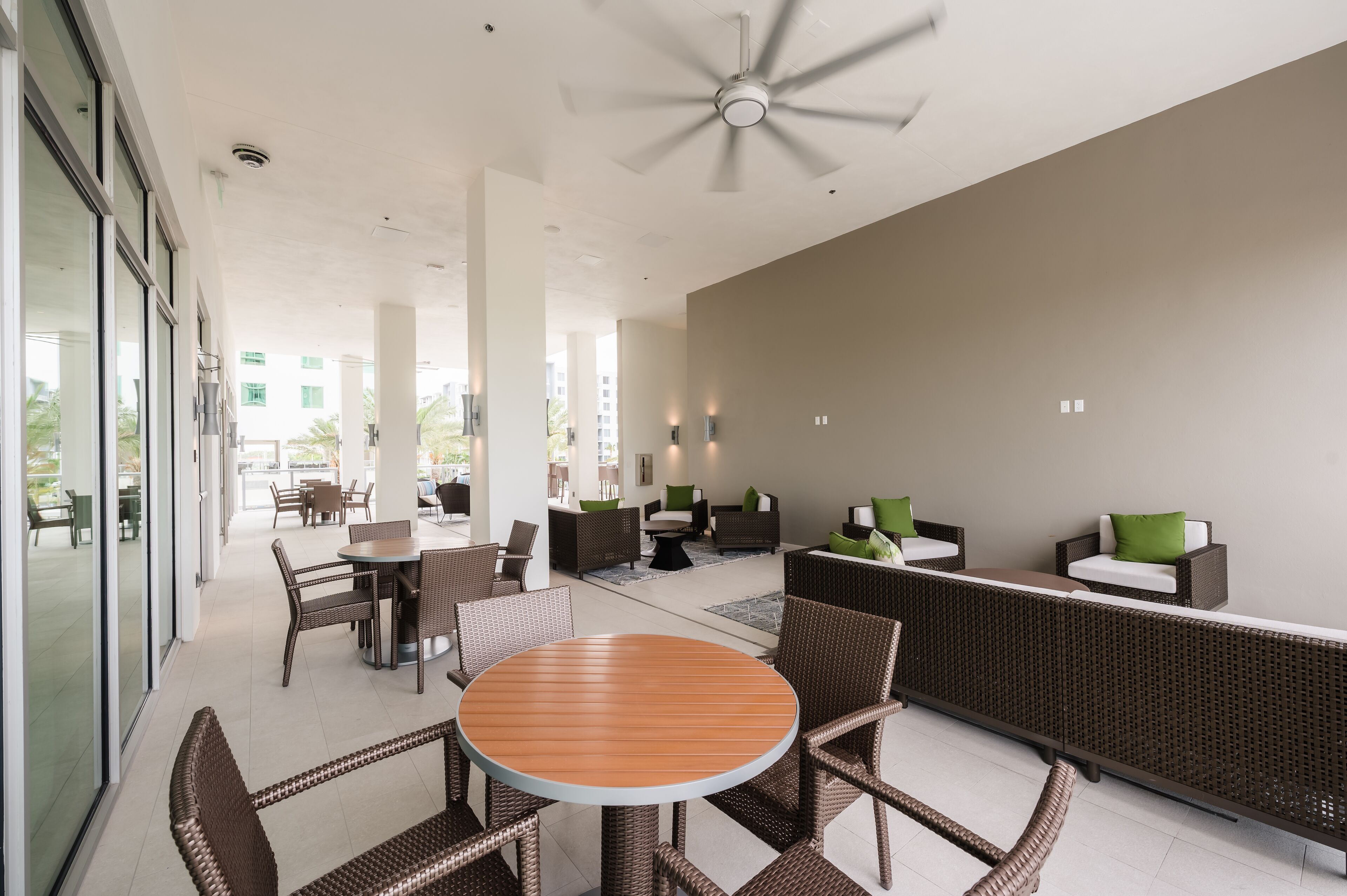 A modern outdoor lounge area with wicker furniture, a round wooden table, and a ceiling fan.