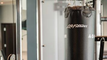 A gym with a punching bag hanging from a metal frame, a weight stack, and a mirror.