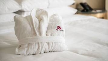 A neatly folded white bathrobe with a logo on it, placed on a bed with white bedding.