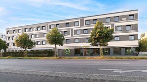 A modern hotel building with a reception area, multiple floors, and a parking lot in front. - B&B Hotel Potsdam (Potsdam)