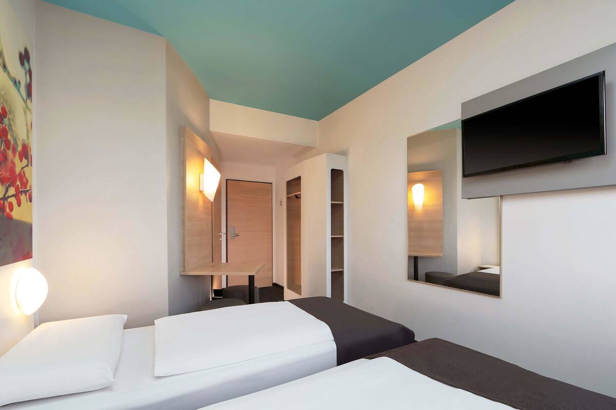Una habitación de hotel con dos camas, un televisor montado en la pared y un cuadro.