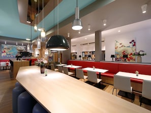 A modern restaurant interior with a long wooden bar, red seating, and contemporary lighting fixtures. - B&B Hotel Potsdam (Potsdam)