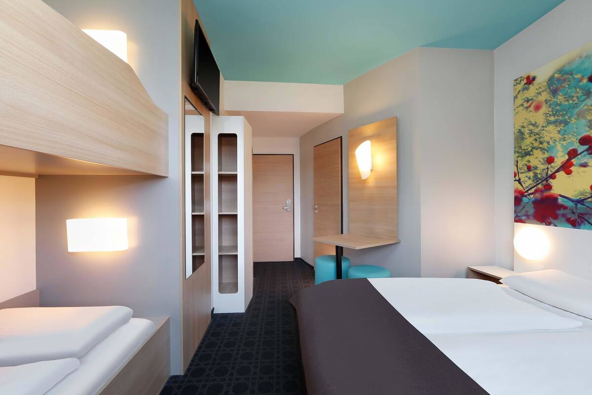 Una habitación de hotel moderna con cama, zona de estar, televisor y un amplio ventanal.