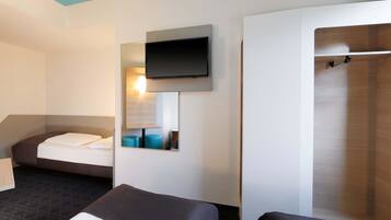 A modern hotel room with a bed, a sofa, a TV mounted on the wall, and a mirror reflecting the room.