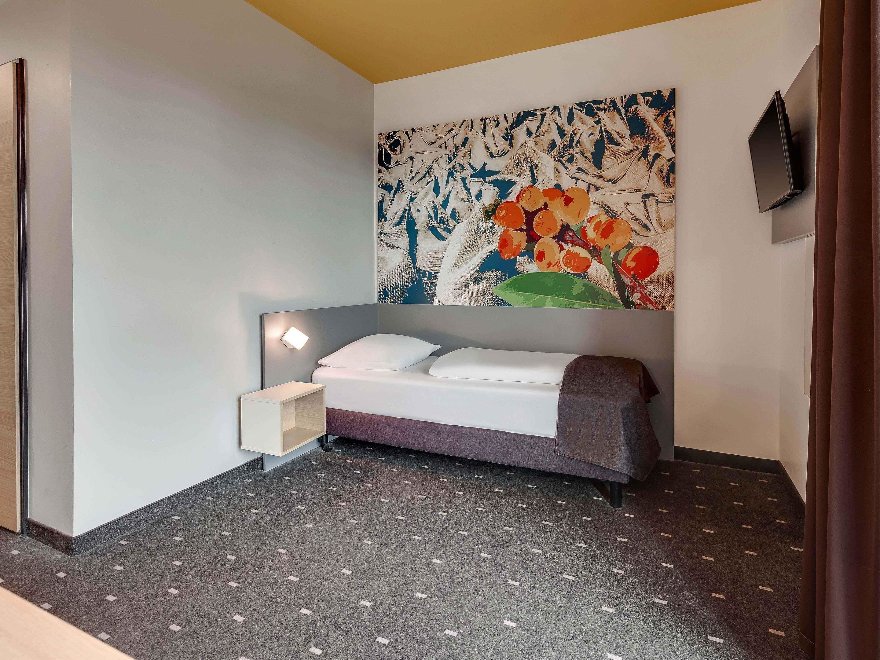 A modern hotel room with a bed, a nightstand, a wall-mounted TV, and a large abstract painting.