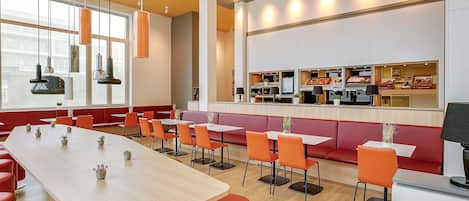 A modern restaurant with a long communal table, individual booths, and a counter with food displays.