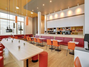Un restaurante moderno con una larga mesa compartida, cabinas individuales y un mostrador con exhibición de alimentos.