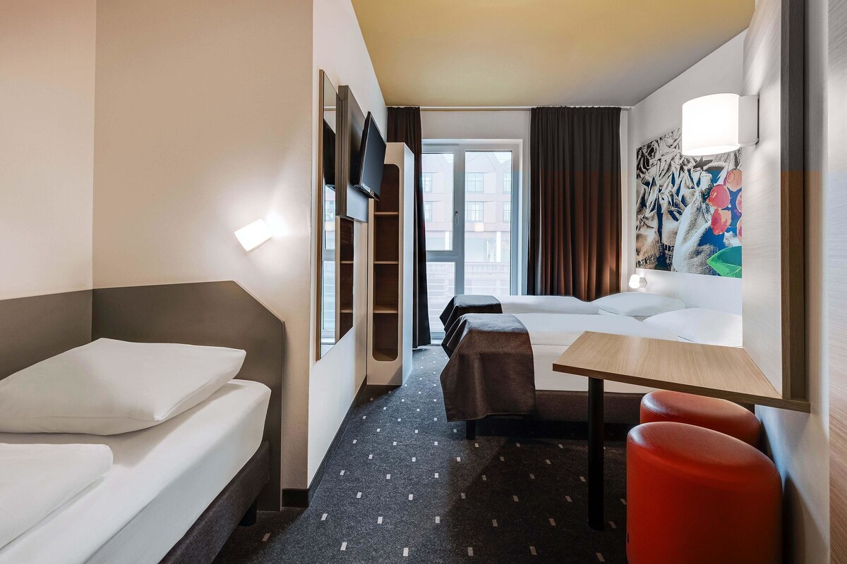 A hotel room with a bed, a desk, a chair, a sofa, and a TV.