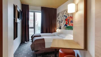 Habitación de hotel con cama, dos mesitas de noche, escritorio, silla, televisión y ventana con cortinas.