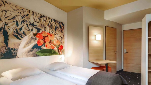 Una habitación de hotel con una cama grande, un escritorio pequeño, un espejo y un armario.