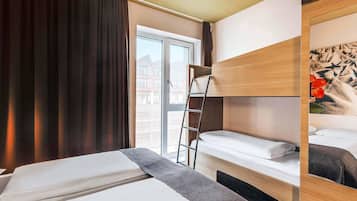A hotel room with a bed, a ladder, a window, and a view of buildings outside.