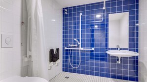 A modern bathroom with a white toilet, a shower with a handheld showerhead, and a sink with a mirror. - B&B Hotel Bremen-Überseestadt (Bremen)