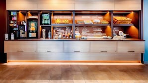 A breakfast bar with a variety of food items and beverages, including a coffee machine and a fruit display. - B&B Hotel Bremen-Überseestadt (Bremen)