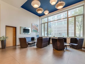 A modern waiting area with a large window, ceiling lights, a flat-screen TV, and seating. - B&B Hotel Bremen-Überseestadt (Bremen)