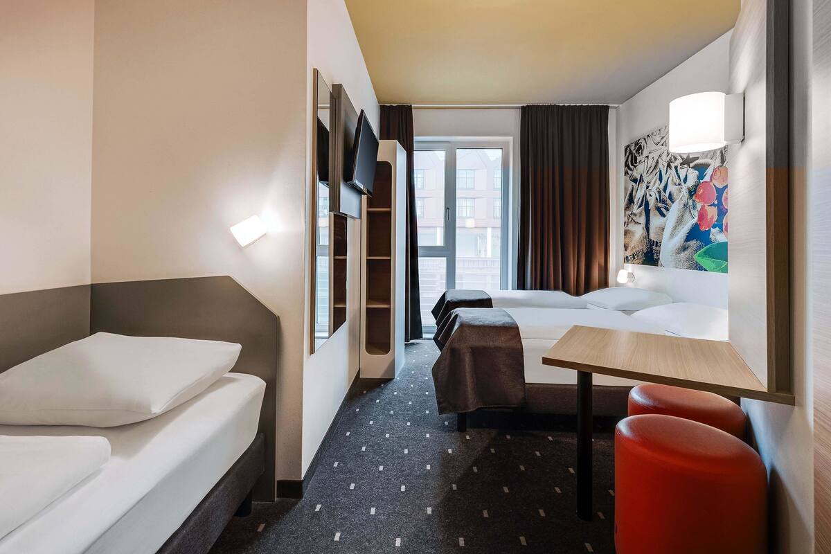 A hotel room with a bed, a desk, a chair, a sofa, and a TV.