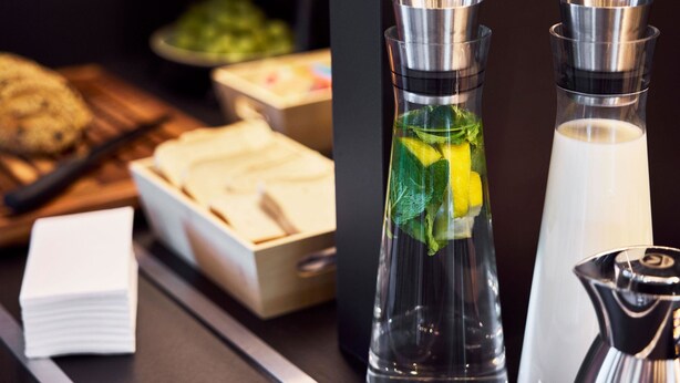 A buffet setup with various food items and two clear glass bottles with a metallic cap, likely containing beverages. - B&B Hotel Bremen-Überseestadt (Bremen)