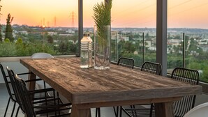Une table en bois, des chaises et un vase en verre contenant une plante, le tout placé devant un paysage au coucher du soleil.