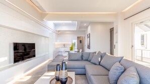 Un salon moderne avec un grand canapé d’angle gris, un téléviseur à écran plat fixé au mur et une table basse agrémentée de vases décoratifs.