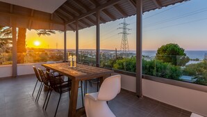 Un espace repas avec une table et des chaises en bois, de grandes fenêtres offrant une vue sur la mer et le paysage urbain.