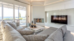 Un salon moderne doté d’un grand canapé d’angle gris, d’un téléviseur à écran plat fixé au mur et d’une cheminée avec un présentoir à bûches.