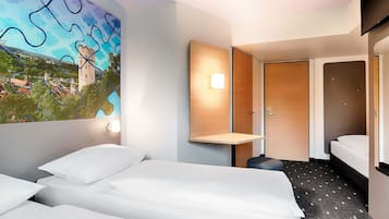 Une chambre d’hôtel avec deux lits, une porte en bois, une lampe fixée au mur et une grande fenêtre donnant sur un château et un paysage.