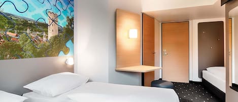 A hotel room with two beds, a wooden door, a wall-mounted light, and a large window with a view of a castle and landscape.