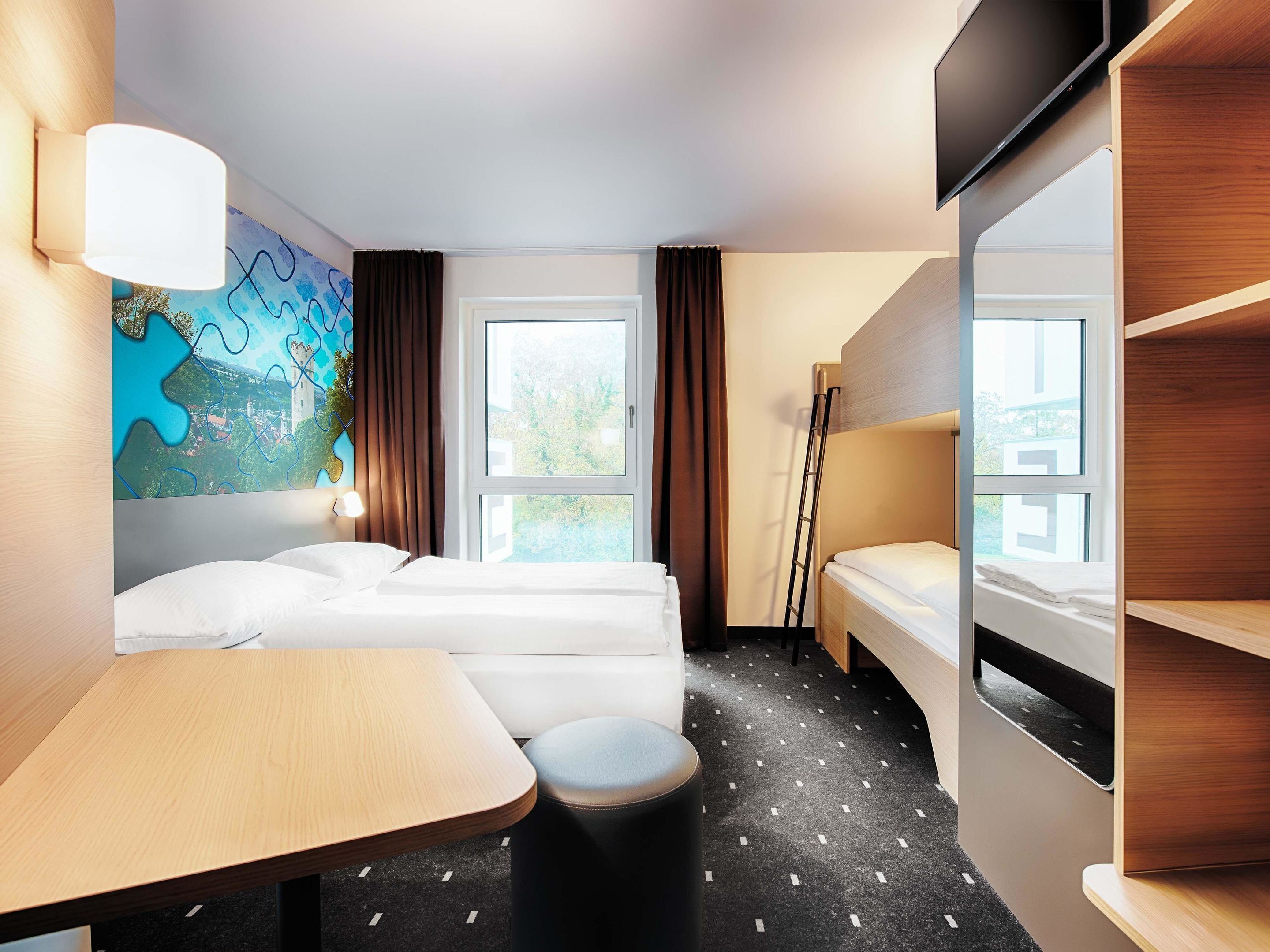 Une chambre d’hôtel avec un lit, un bureau, une chaise, une télévision et une fenêtre avec des rideaux.