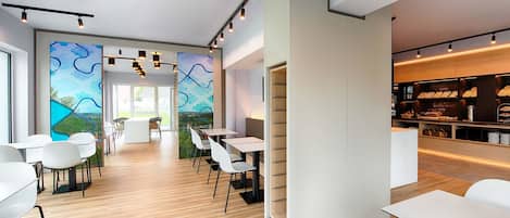 Un espacio de oficina moderno con mobiliario blanco, un mural con diseños abstractos y una zona de café con un expositor de menú.