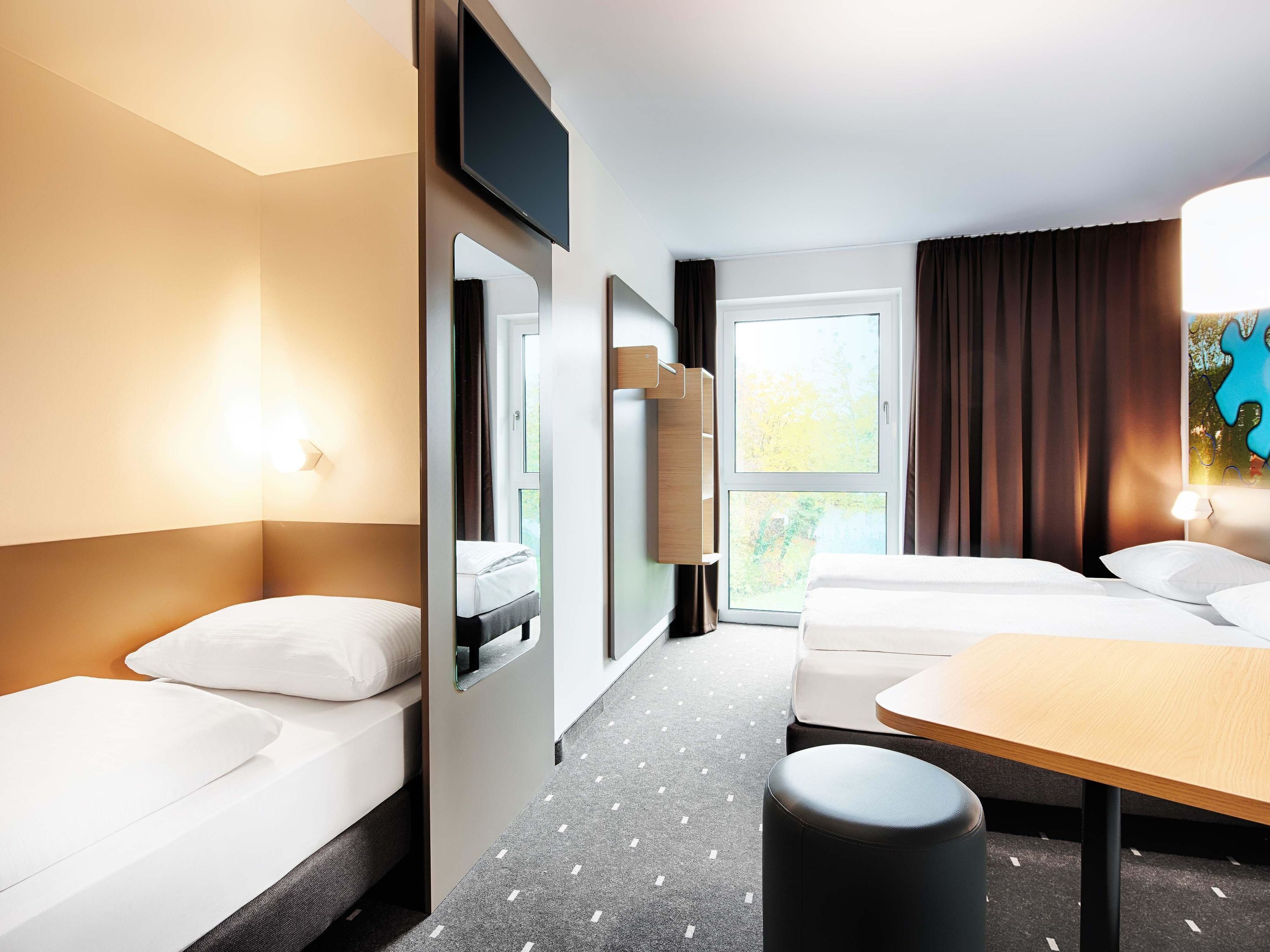 Une chambre d’hôtel avec deux lits, un bureau, une télévision et une fenêtre avec des rideaux.