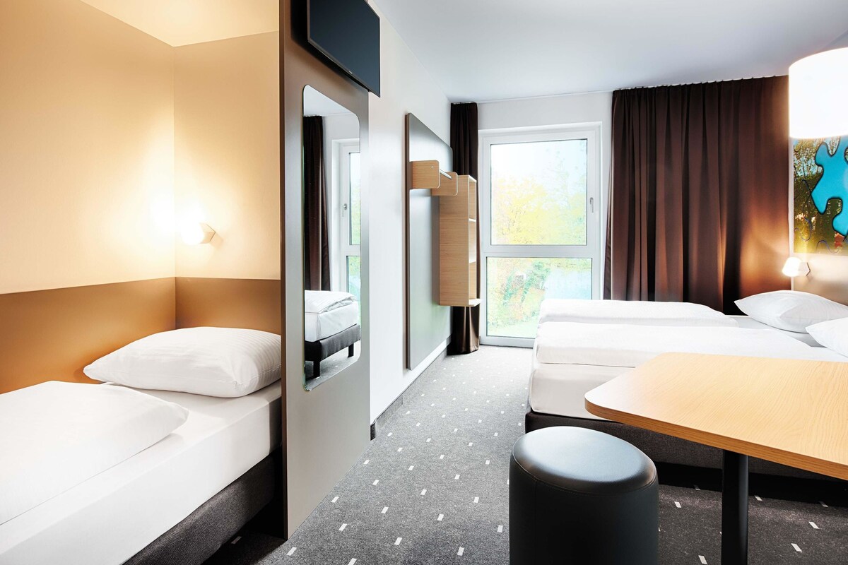 A hotel room with two beds, a desk, a TV, and a window with curtains.
