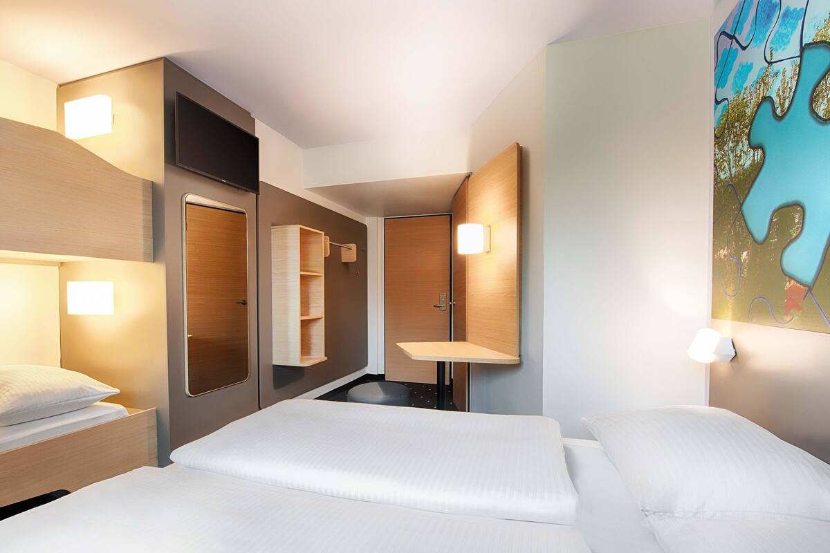 A hotel room with two beds, a large mirror, a wooden headboard, and a wall-mounted light fixture.