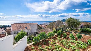 Un barrio residencial con casas adosadas, un jardín con plantas y vistas al mar y colinas al fondo.