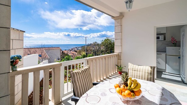 Un balcón con mesa lista para el desayuno, vista al mar y una zona de cocina.