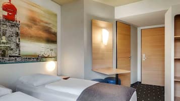 Habitación de hotel con dos camas, un cuadro grande en la pared, una puerta de madera y una mesita.
