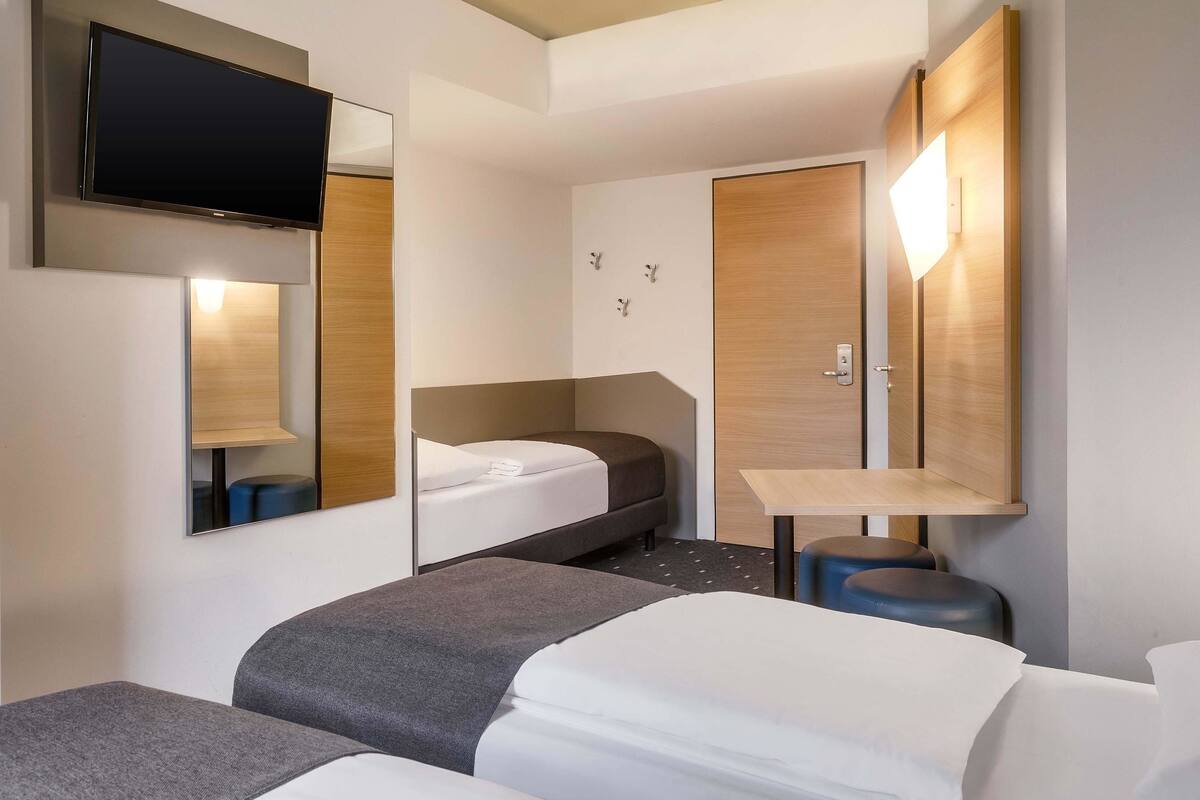 Une chambre d’hôtel moderne équipée d’un lit, d’un bureau, d’une chaise et d’un téléviseur fixé au mur.