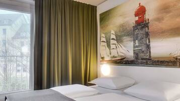 Una habitación de hotel con una cama, un ventanal con cortinas y un cuadro de un faro.