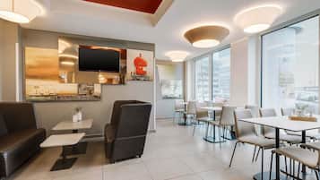 A modern dining area with a flat-screen TV, artwork, and a mix of seating options including tables and chairs.